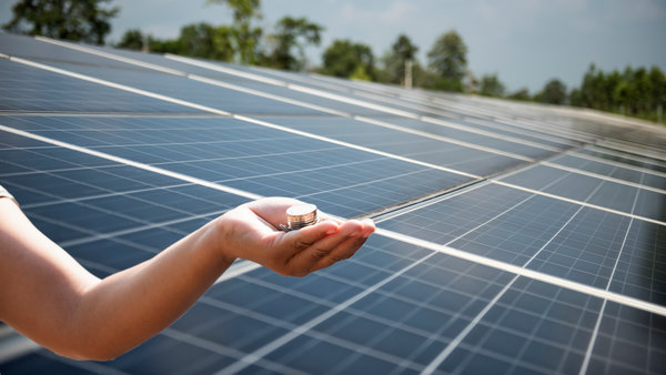 Auf dem mit Solarpanelen ausgestatteten Hausdach ist eine Hand, mit Münzen
